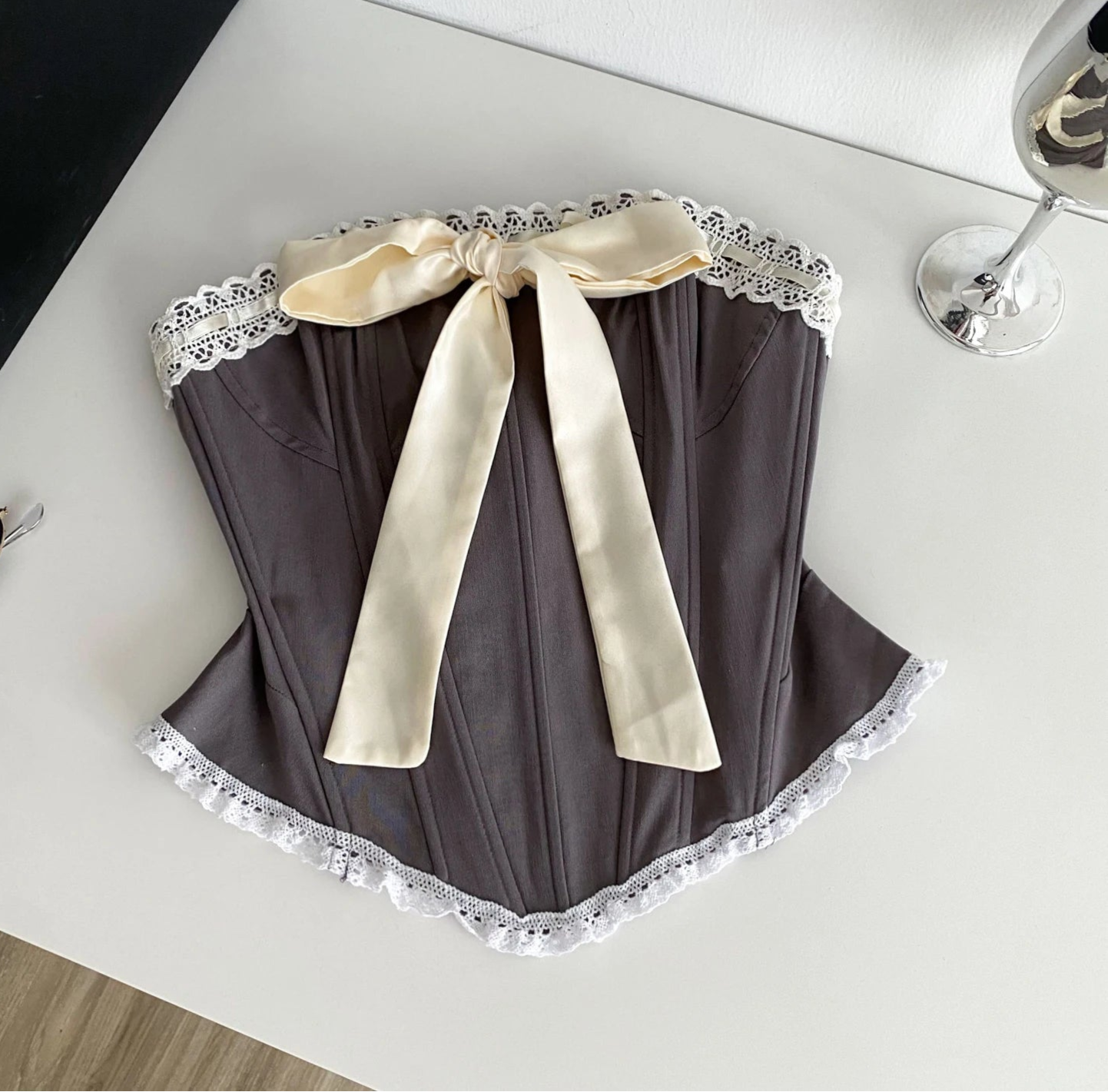 Brown lace-trimmed garment with a cream ribbon on a white surface.