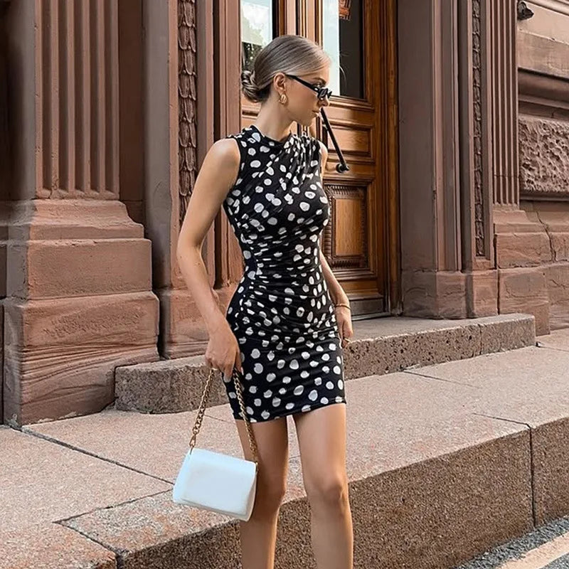 Woman in a black and white polka dot dress standing on steps in front of a building.