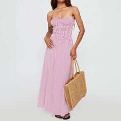 Woman wearing a pink and white striped dress holding a woven bag on a plain background