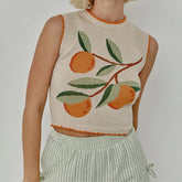 Person wearing a sleeveless knitted top with orange and green design on a plain background
