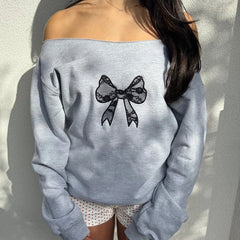Gray sweatshirt with a black bow design worn by a person against a neutral background