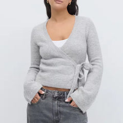 Woman wearing a gray wrap sweater over a white top and jeans on a light gray background