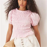 Woman wearing a pink smocked top with white pants against a plain background