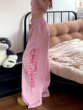 Person wearing pink sweatpants with a design in a bedroom