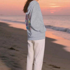 Person wearing a gray hoodie with colorful designs on a beach at sunset