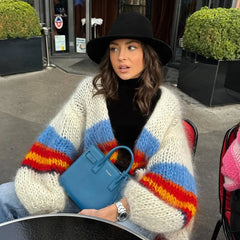 Woman wearing a colorful striped sweater and black hat, holding a blue handbag.