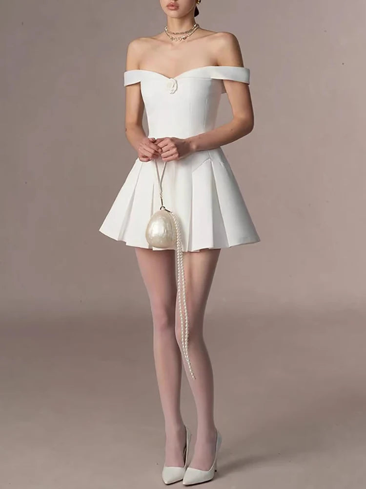 Woman wearing a white off-shoulder dress with sheer stockings and a pearl-handled bag on a beige background