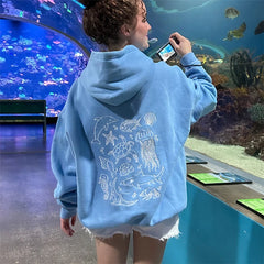 Person wearing a blue hoodie with sea creature designs, taking a photo of an aquarium.