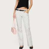 Person wearing polka dot pants with a black belt and holding a pink bag on a white background