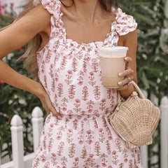 Woman in a floral dress holding a drink and a woven bag outdoors.