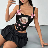 Woman wearing a black top with pink bows and floral design, sitting on a gray surface.