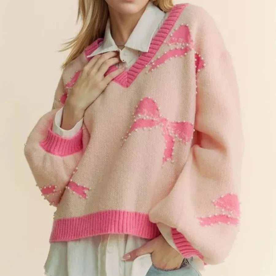 Person wearing a pink and beige sweater with a pattern of pink bows on a beige background