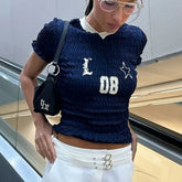 Woman wearing a navy blue textured top with lettering, holding a black bag.