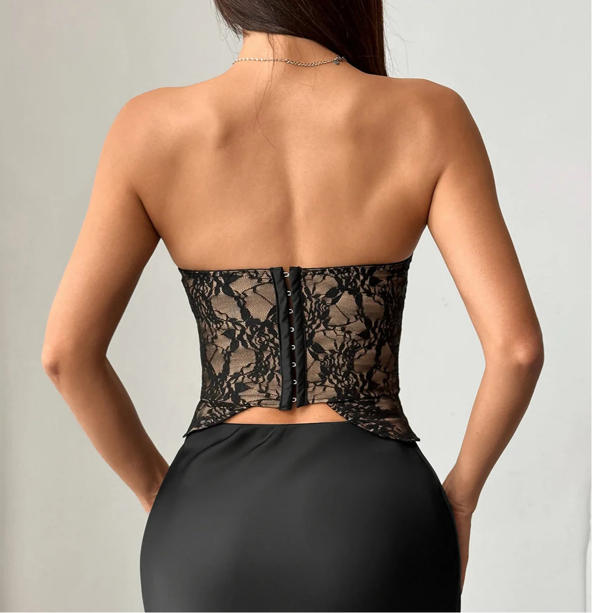 Black lace corset worn by a model on a plain background