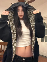 Person wearing a black hoodie with leopard print lining, white top, and black pants indoors.