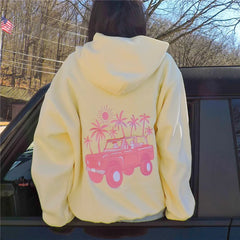 Person wearing a yellow hoodie with pink graphic design, standing next to a car outdoors.