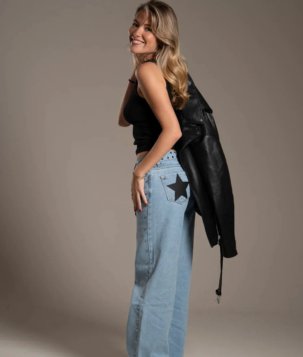 Woman wearing a black leather jacket and light blue jeans with a star design
