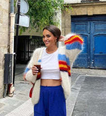 Woman in colorful cardigan and blue pants standing on a street with a blue door in the background