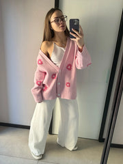 Person wearing a pink cardigan with floral patterns in front of a mirror.