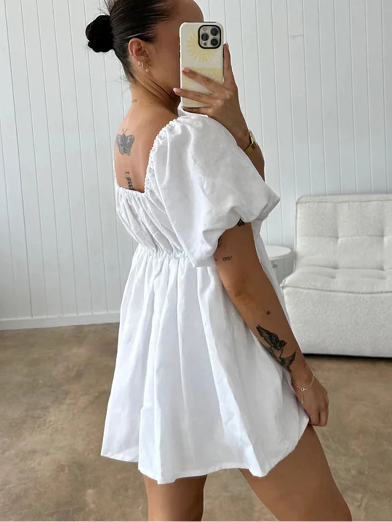 Woman wearing a white dress taking a mirror selfie in a room with a white couch.