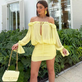 Woman wearing a yellow off-shoulder outfit with matching handbag in front of green plants.