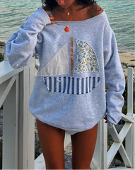 Person wearing a gray sweatshirt with patchwork design by the beach