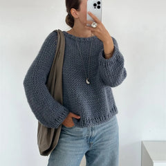 Person wearing a blue knitted sweater and jeans, holding a phone and a bag.