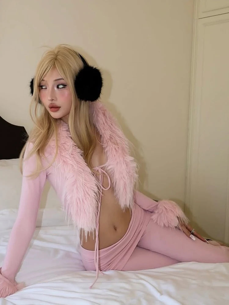 Person wearing a pink outfit with a feathered shrug and black earmuffs on a bed.