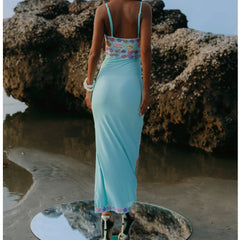 Woman in a light blue dress standing on a rocky beach.