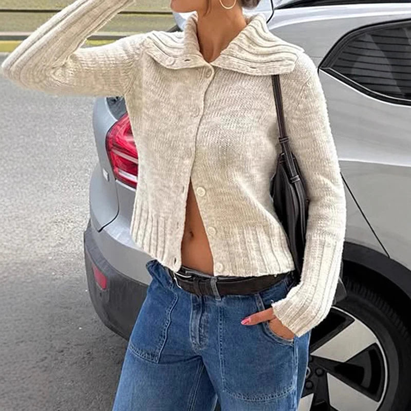 Person wearing a cream knitted cardigan and blue jeans standing next to a car.