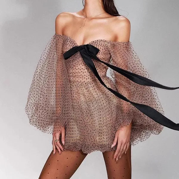 Woman wearing a sheer off-shoulder dress with a black ribbon on a gray background
