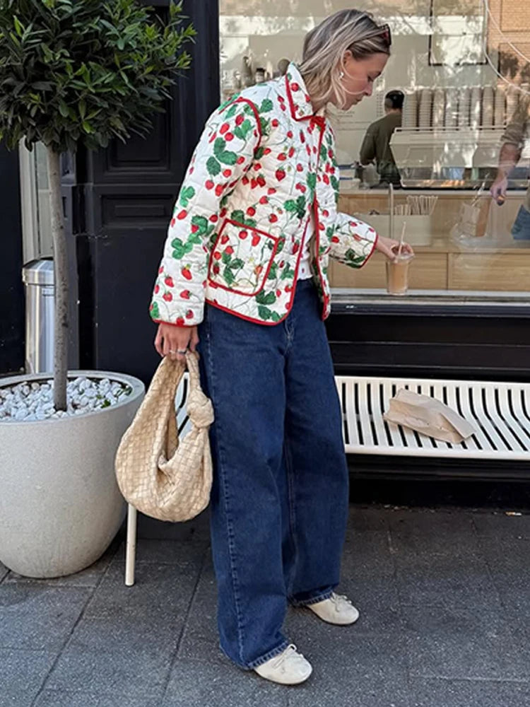 Person wearing a colorful patterned jacket and blue jeans standing outside a building.
