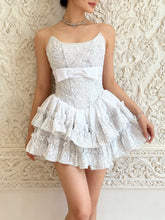 White lace dress with a bow belt worn by a person against an ornate wall.