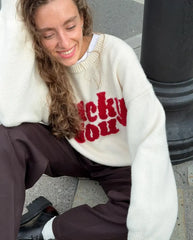 Person wearing a white sweater with red text sitting on the ground.