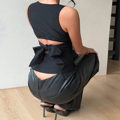 Person wearing a black sleeveless top with a bow and high-waisted black pants, sitting on a chair.