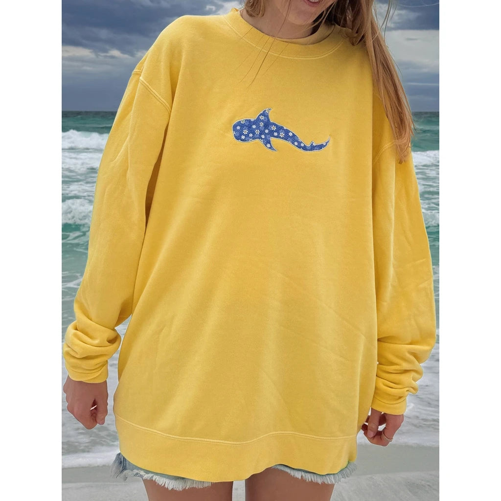 Person wearing a yellow sweatshirt with a blue whale design on a beach.