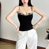 Woman wearing a black top with zebra pattern straps and white pants indoors.