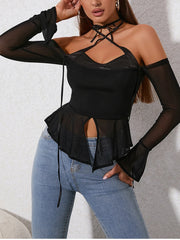 Woman wearing a black top with sheer sleeves and cut-out design, paired with blue jeans on a light gray background.