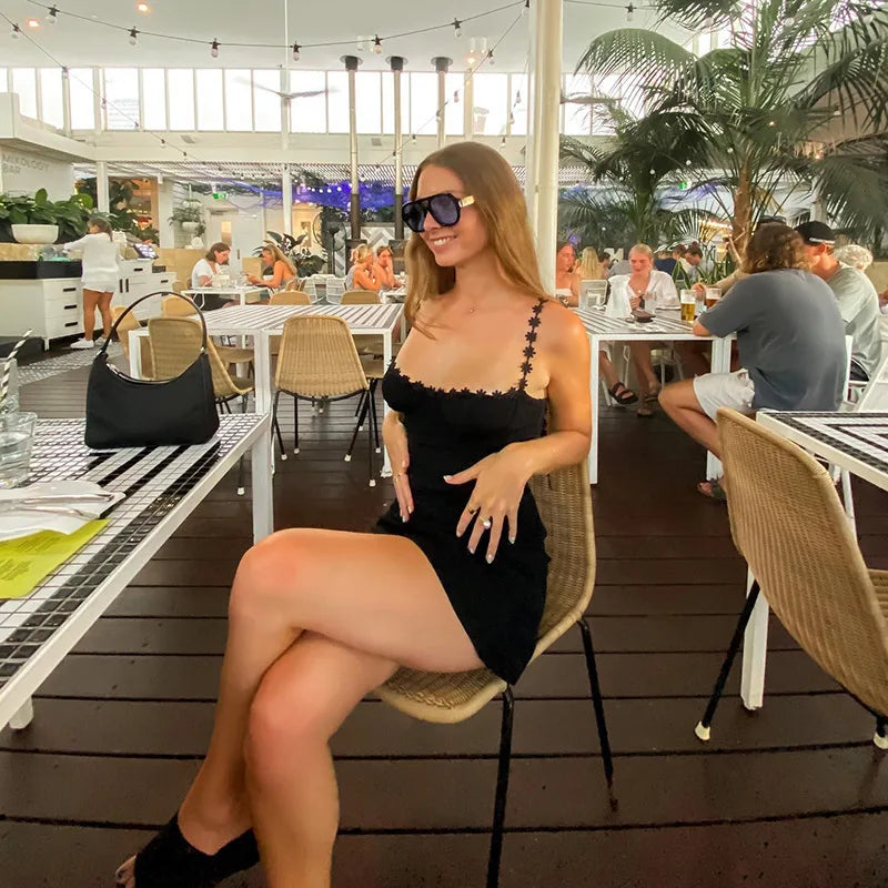 Woman in a black dress sitting at an outdoor cafe with palm trees in the background