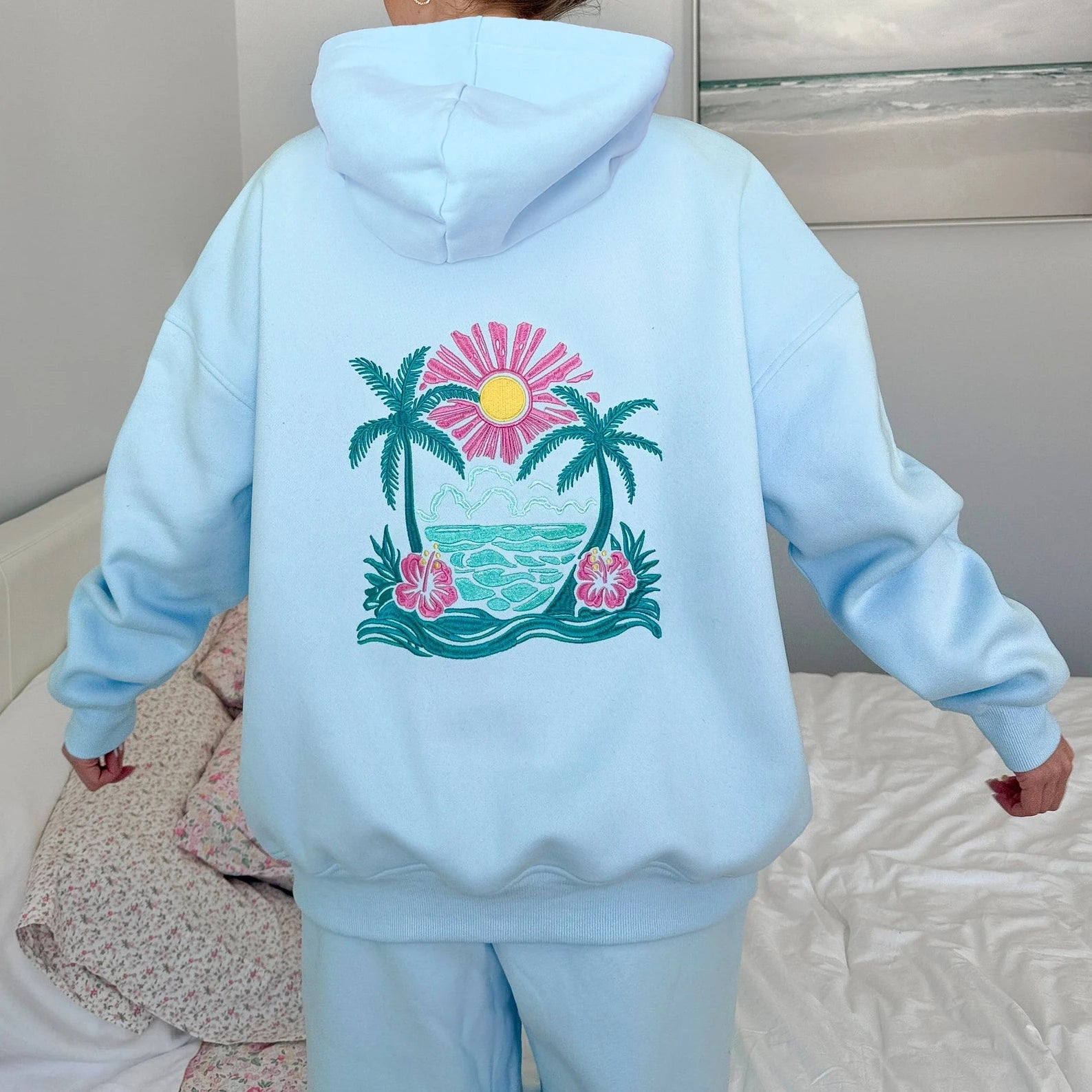 Light blue hoodie with a tropical design on the back worn by a person.