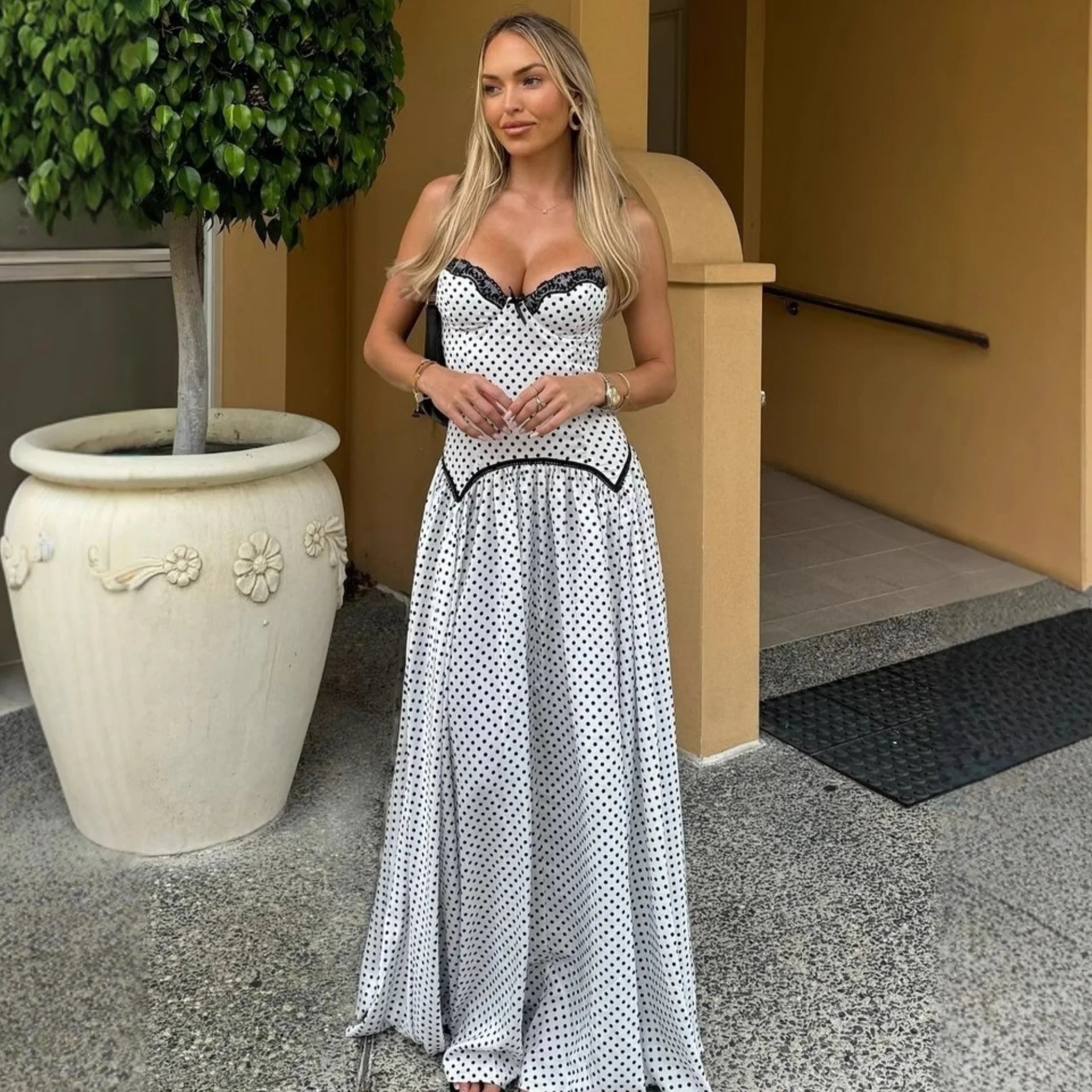 Woman in a polka dot dress standing outdoors next to a large planter.