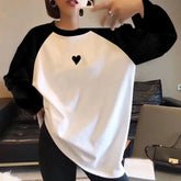 Person wearing a black and white long-sleeve shirt with a heart design, taking a mirror selfie.