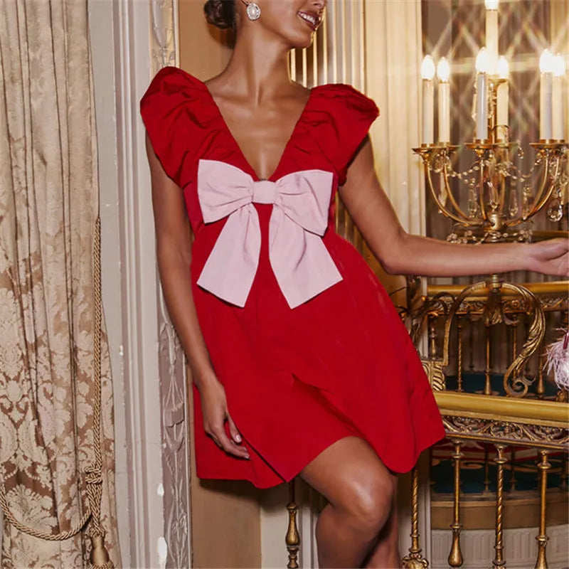Woman wearing a red dress with a large pink bow in an elegant interior setting.