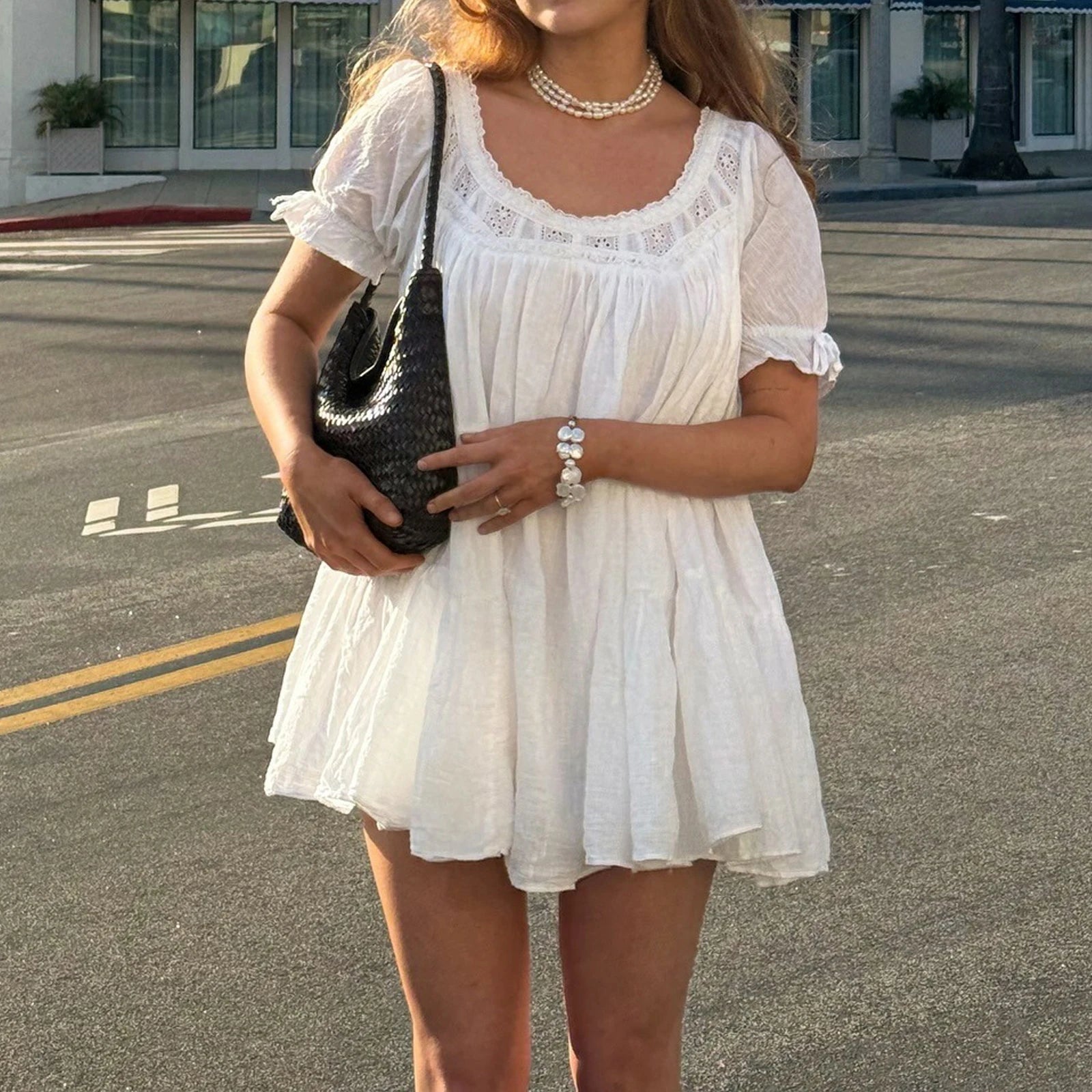 Woman in a white dress holding a black handbag on a street.