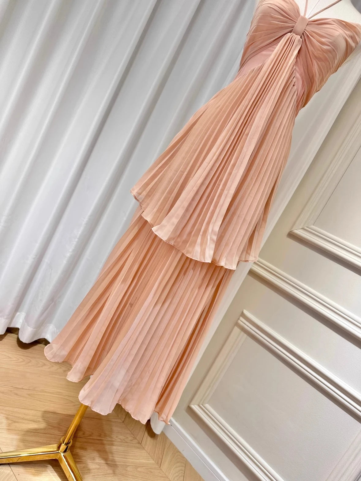 Pink pleated dress on a mannequin against a white curtain background