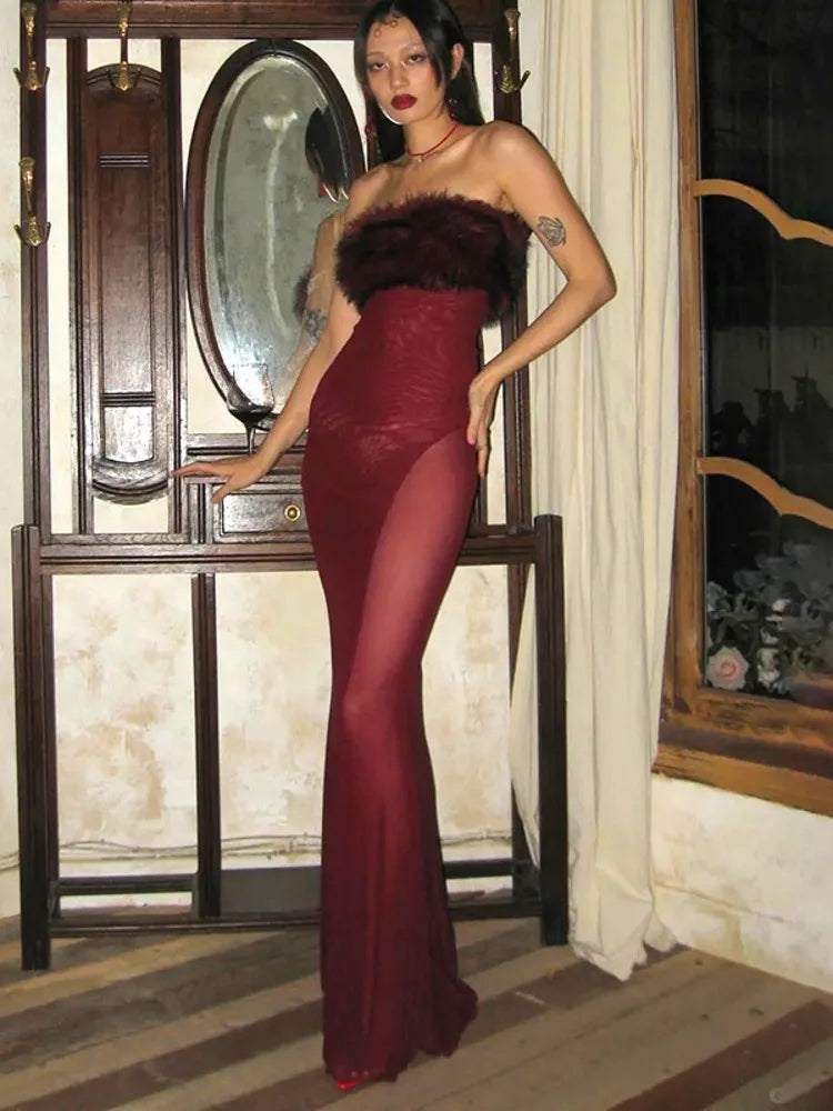 Woman in a burgundy evening gown with fur trim standing in an elegant interior setting.