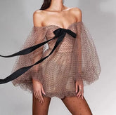 Woman wearing a sheer polka dot dress with a black ribbon on a gray background