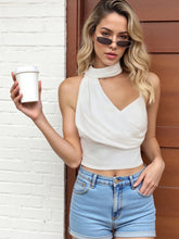 Woman in a white top and blue shorts holding a coffee cup against a white brick wall.