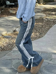 Person wearing blue jeans with white stripes and brown shoes on a stone pathway.