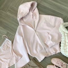 Light pink hoodie, tank top, and shorts laid out on a wooden floor.